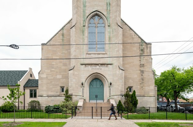 buitenkant van de kerk met zwarte poort en persoon die voorbij loopt