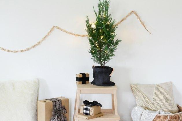 uma pequena árvore de natal em vaso decorada com algumas luzes está em um banquinho
