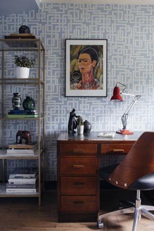 amžiaus vidurio modernus namų biuras, kuriame mėlynos spalvos tapetai ir mįslės su mįsle, virš stalo rašomas Frida khalo portretas