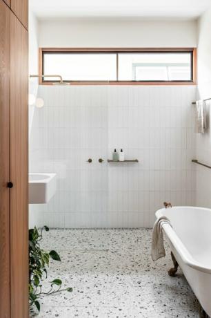banheiro moderno branco com piso de terrzzo e uma banheira com pés ao lado de um chuveiro