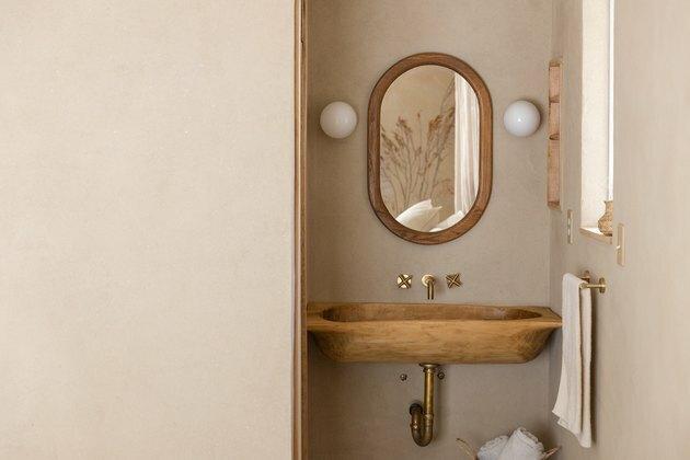 pia de parede de madeira, espelho retangular com acabamento em madeira, dois arandelas de luz redondas brancas, barra de toalha com toalha rosa