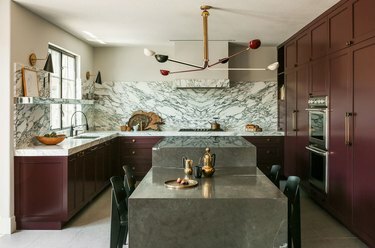 cocina con gabinetes granate, isla de piedra de color topo, placa para salpicaduras de mármol y paredes beige