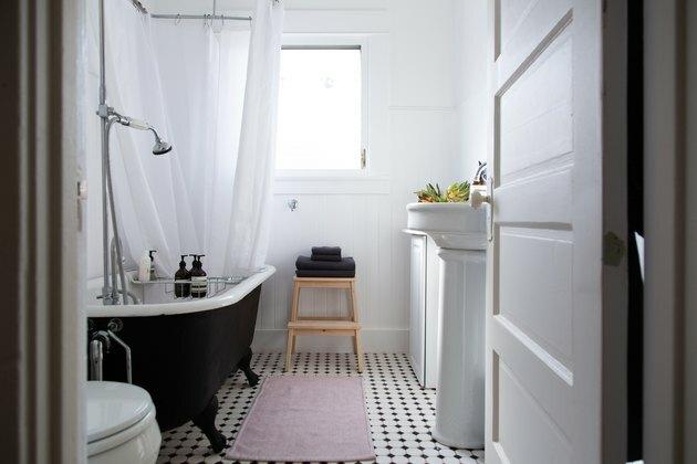 banheiro com pia de pedestal, banheira preta com pés de garra e piso de xadrez