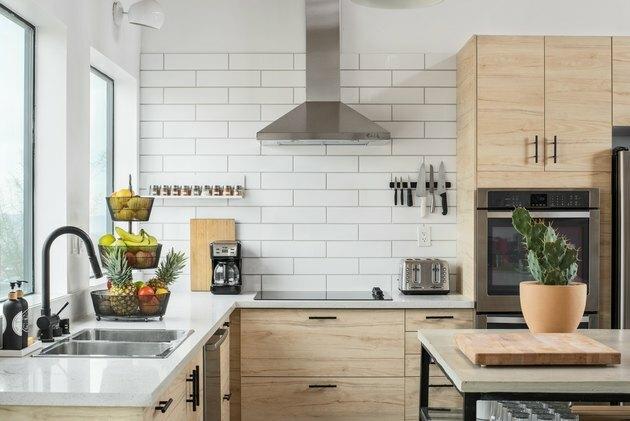 colț de bucătărie cu pereți din gresie albă, ferestre mari, chiuvetă, dulapuri din lemn pal