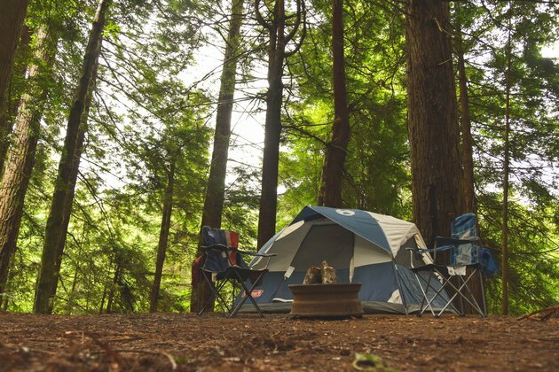 acampamento com barraca de camping, duas cadeiras de camping e fogueira