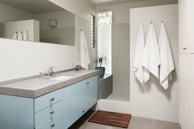 vaidade do banheiro azul e cinza com pia, chuveiro walk-in e três toalhas em ganchos