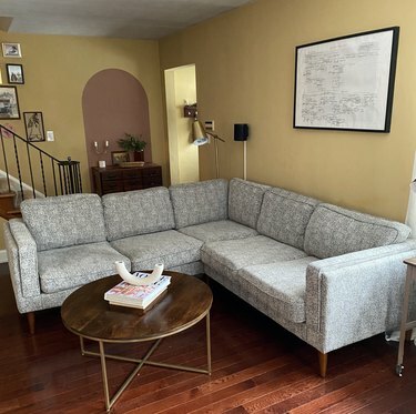 Um corte cinza em uma sala amarela; uma mesa de café redonda marrom com livros