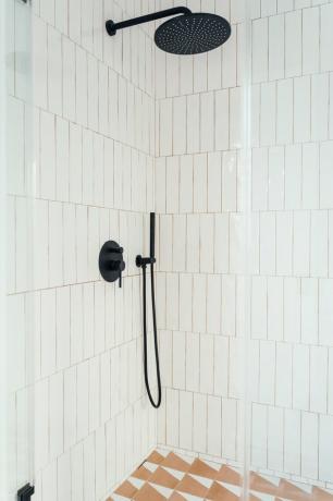 ușă de duș din sticlă cu gresie albă verticală, cap de duș și accesorii negre, pardoseală cu gresie cu model triunghiular portocaliu