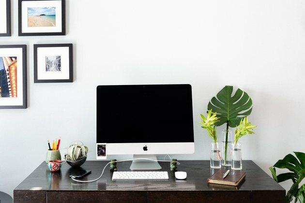 mesa com computadores, plantas, decoração e porta-retratos da apple