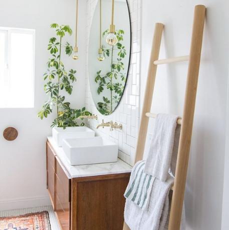 Banheiro com toalheiro com escada de madeira, penteadeira de madeira, pias de vasos, planta, espelho redondo e idéias escandinavas de armazenamento de banheiro