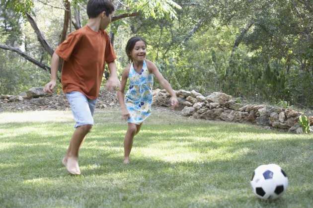 Priekinis berniuko ir mergaitės, žaidžiančio futbolą sode, profilis