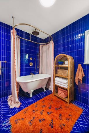 Azulejo de chuveiro azul do chão ao teto em banheiro moderno com tapete laranja