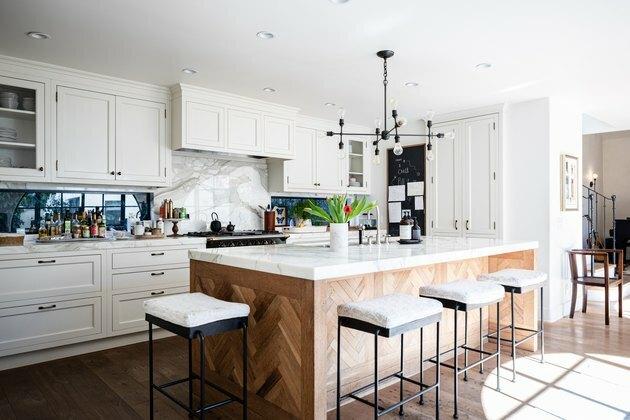 cozinha com armários brancos, ilha de cozinha de madeira decorativa com pia e bancos brancos