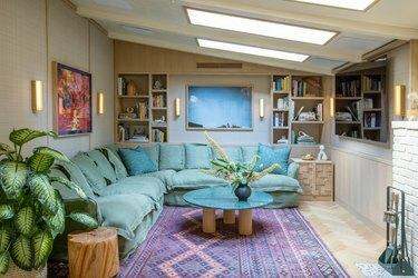 ruang media dengan sofa sectional pirus dan permadani ungu di bawah skylight
