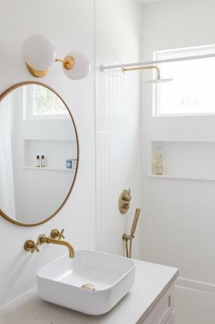 Um banheiro minimalista branco com detalhes em ouro e pia moderna de meados do século