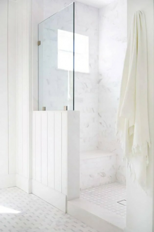 Chuveiro costeiro com vidro, shiplap e uma parede de mármore branco
