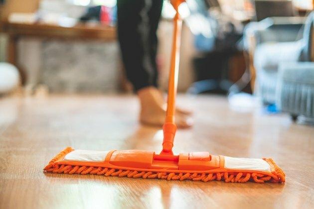 Hombre soltero sosteniendo un trapeador y limpiando el piso laminado en casa