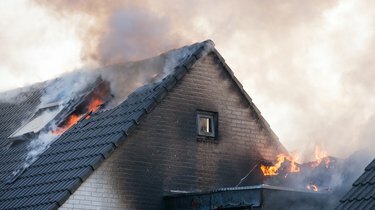 Fragment domu ze zašpiněných bílých cihel, který hoří plameny a kouří ven
