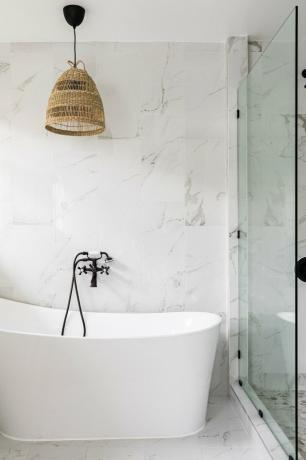 Banheiro minimalista com banheira, box de vidro e luminária de vime