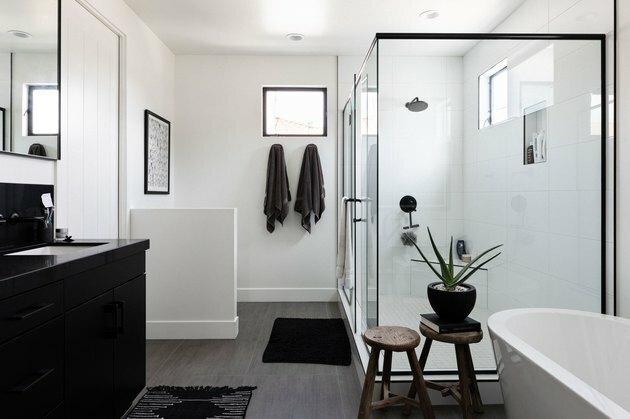 banheiro amplo com banheira branca independente, dois bancos de madeira, toucador preto, chuveiro de vidro com detalhes em preto, duas toalhas desligadas, piso de madeira