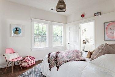 लकड़ी के फर्श और गुलाबी लहजे के साथ सफेद दीवारों वाला बेडरूम
