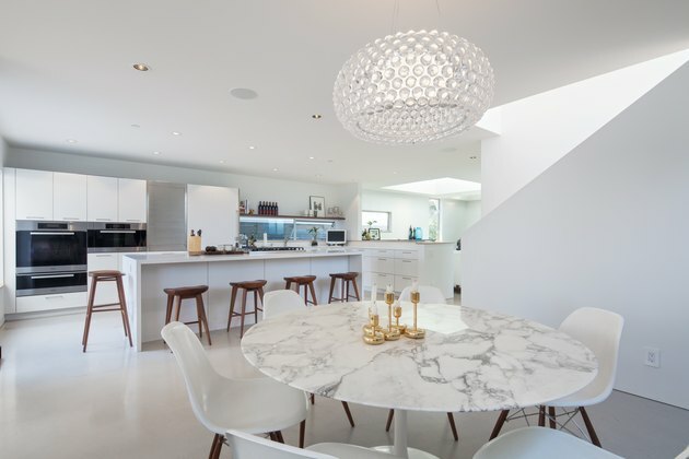 Uma mesa de jantar Saarinen Tulip de mármore é cercada por cadeiras laterais de fibra de vidro moldadas Herman Miller Eames na área de jantar.