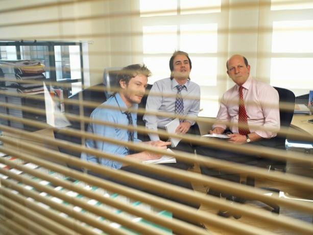 Drie zakenlieden in vergadering, bekijken door glaspaneel
