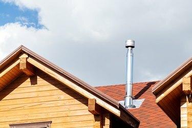 צינור ארובה מנירוסטה על גג בית וילה קוטג 'מודרני עם קורות עץ. אח ביתית ומערכת פליטה לחימום