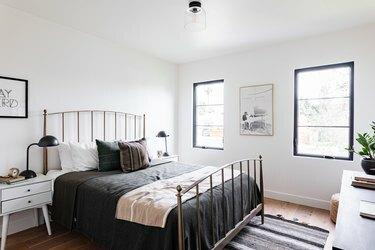 Un dormitor cu balustradă de pat din fier, un covor și o comodă albă