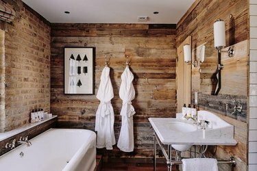 Kupaonica s bijelom kadom i sudoperom, pregrađenim drvenim dijelom, zidom od opeke.