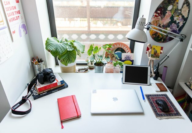 Mesa branca com caderno vermelho e laptop fechado contra a janela