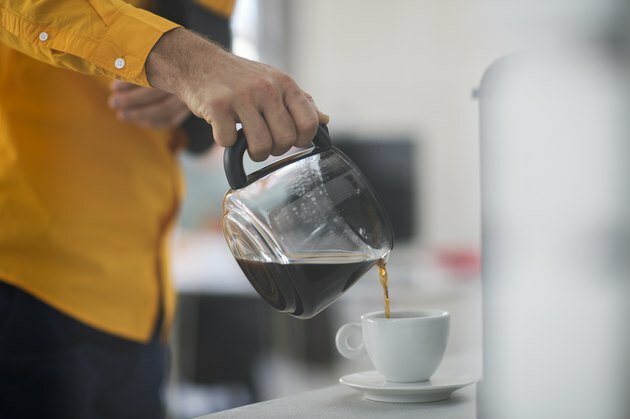 Werknemer met slinger gieten koffie in de beker op het werk