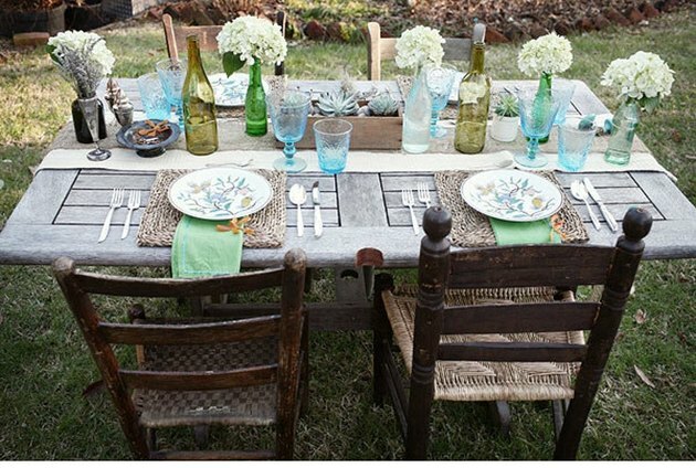 Porta de celeiro vintage adaptada como mesa de jantar com duas cadeiras de madeira e mesa posta com flores e copos