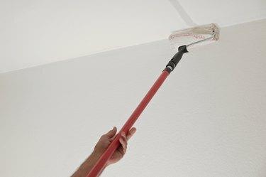 Рука човека који држи ваљак за фарбање на дугачком телескопском стубу да фарба плафон док реновира стан, концепт становања, простор за копирање, одабрани фокус