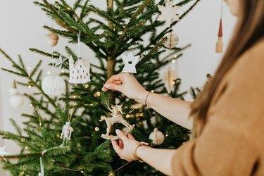 osoba koja stavlja ornament konja za ljuljanje na božićno drvce