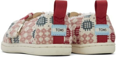 Il retro di un paio di pantofole West Elm x TOMS in un motivo verde, rosa, bianco e rosso con etichette TOMS sui talloni