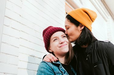 Due donne che indossano berretti rossi e gialli. Uno sta baciando la fronte dell'altro.