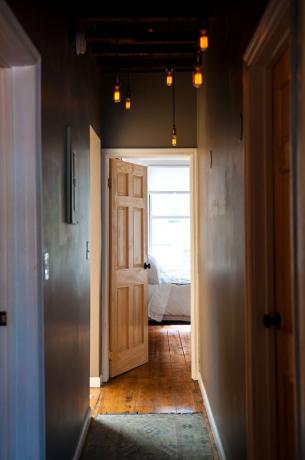 Ideias para iluminação de corredores em um corredor estreito com luzes fracas pendentes e um piso de pinho rústico que se abre para um quarto bem iluminado