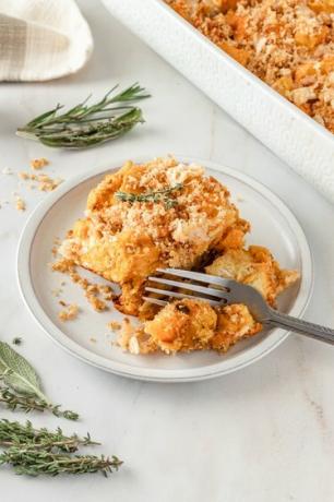 Una zucca gialla e arancione cuocere su un piatto bianco condita con briciole di pane tostato.