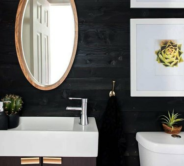 Kupaonica s bijelim umivaonikom, WC-om, ogledalom, crnim zidovima.