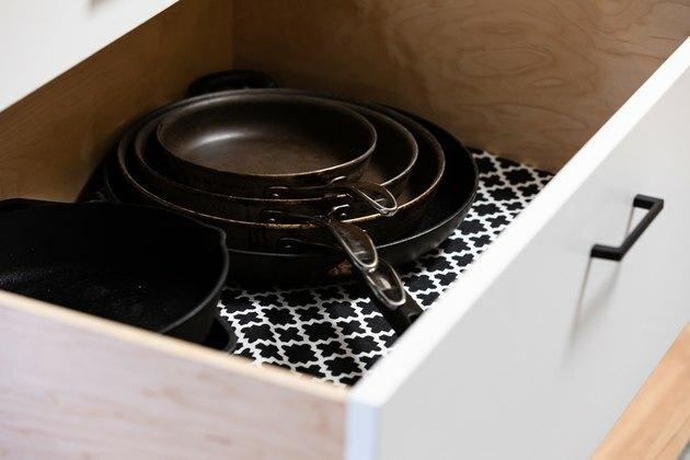 gaveta de cozinha branca forrada com papel estampado e panelas empilhadas