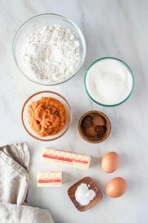 Ciotole di vetro su un ripiano di marmo piene di ingredienti, accanto a bastoncini di burro e due uova.