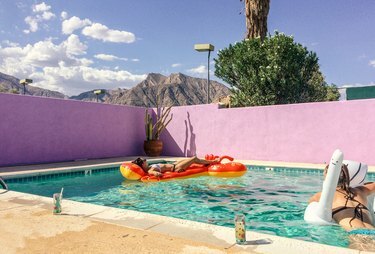 Piscina externa com infláveis ​​lagosta e cisne, paredes de tijolos pintados de rosa e pátio bronzeado contra as nuvens e a montanha