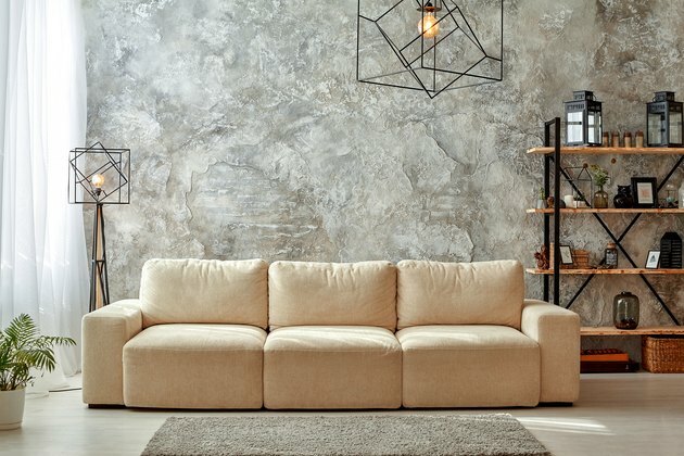 Moderne interiør i stue med grå vægge, beige sofa, gulvlampe og lysekrone, lys tæppehylde med rammer og krukker, blomst i en gryde