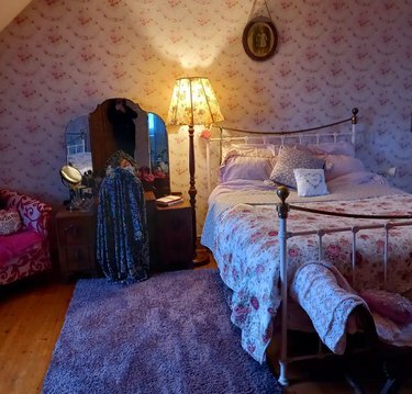 guļamistaba ar ziedu tapetēm, segu un abažūru
