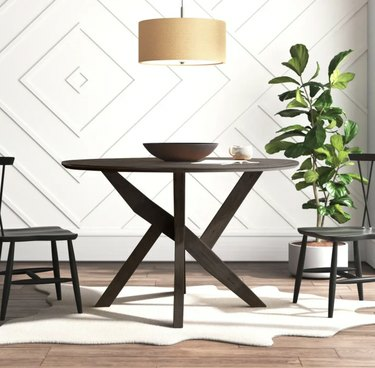 Слика смеђег округлог трпезаријског стола и две столице. У средини стола је чинија, а у углу собе биљка.