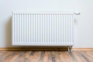 Calentador de radiador casero en la pared blanca sobre piso de madera. Equipo de calentamiento ajustable para apartamento y hogar.
