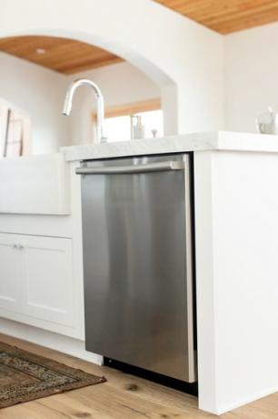 Rustfri opvaskemaskine i hvid køkkenø. Marmorbordpladen strækker sig over opvaskemaskinen. En krom vandhane er synlig.