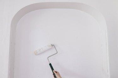 Persoană care folosește o rolă de vopsea pentru a aplica grund pe o nișă de perete arcuită