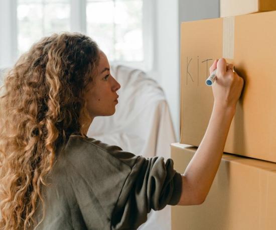 Femme aux cheveux bouclés écrit «cuisine» sur une boîte de déménagement en carton